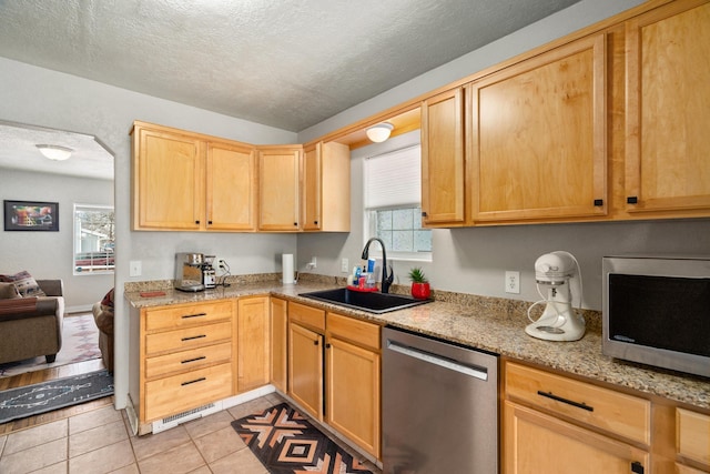 kitchen featuring sink, a textured ceiling, light tile patterned floors, stainless steel appliances, and light stone countertops