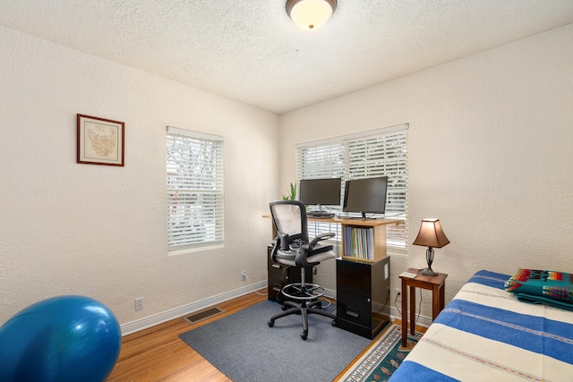 bedroom with multiple windows, wood-type flooring, and a textured ceiling