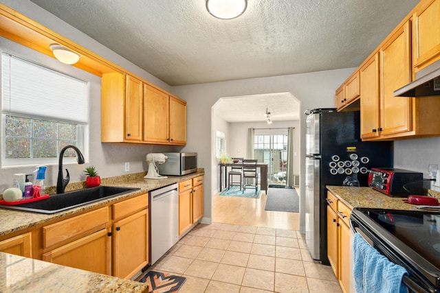 kitchen featuring appliances with stainless steel finishes, sink, light tile patterned floors, light stone countertops, and a textured ceiling