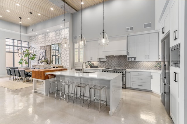 kitchen with white cabinetry, built in appliances, sink, and a center island with sink