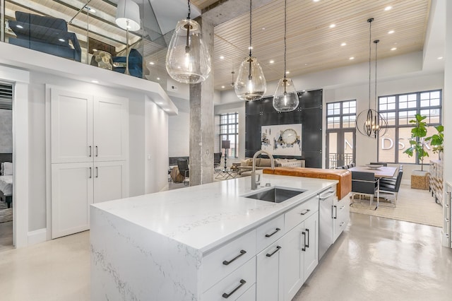 kitchen with sink, decorative light fixtures, a center island with sink, light stone countertops, and white cabinets