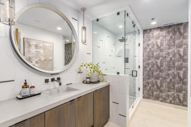 bathroom featuring a shower with door, vanity, and tile walls