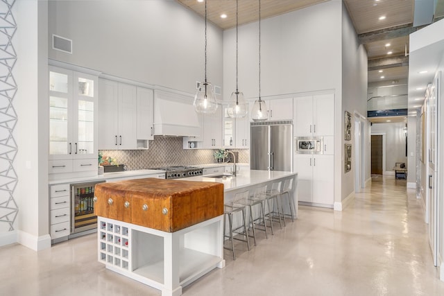 kitchen featuring white cabinetry, beverage cooler, custom exhaust hood, built in appliances, and a center island with sink