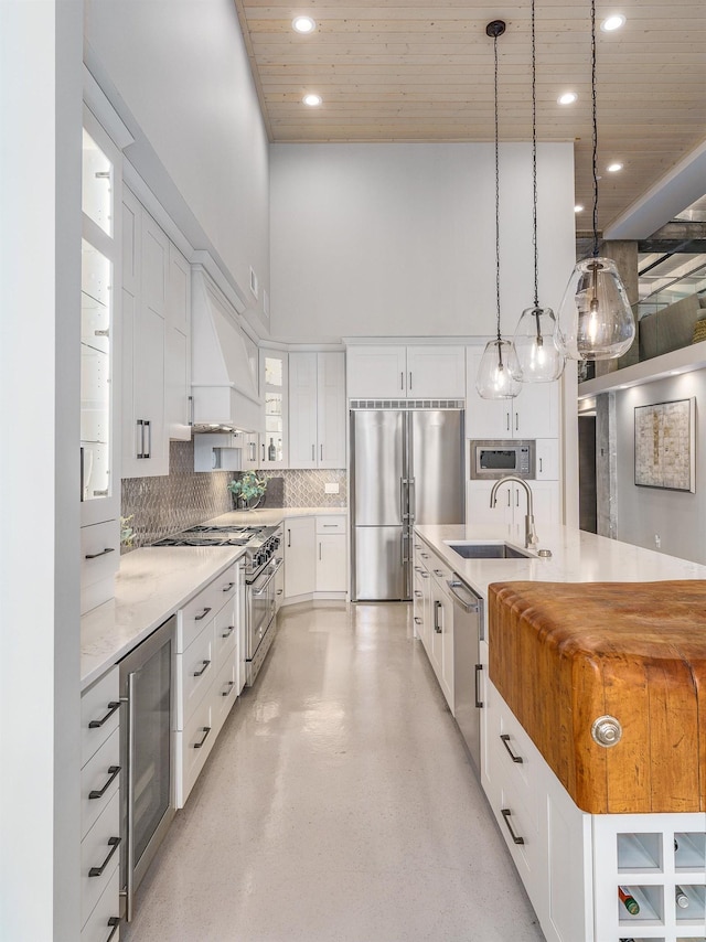 kitchen featuring premium range hood, sink, white cabinetry, built in appliances, and decorative light fixtures