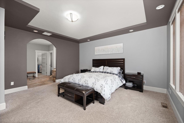 bedroom with a raised ceiling and light colored carpet