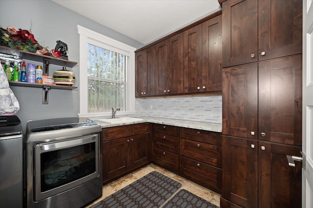 kitchen featuring sink, stainless steel range with electric cooktop, dark brown cabinets, independent washer and dryer, and light stone countertops