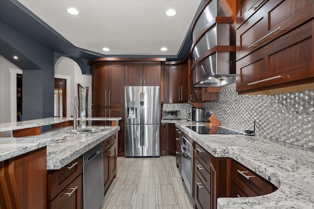 kitchen featuring sink, light stone countertops, stainless steel appliances, range hood, and decorative backsplash