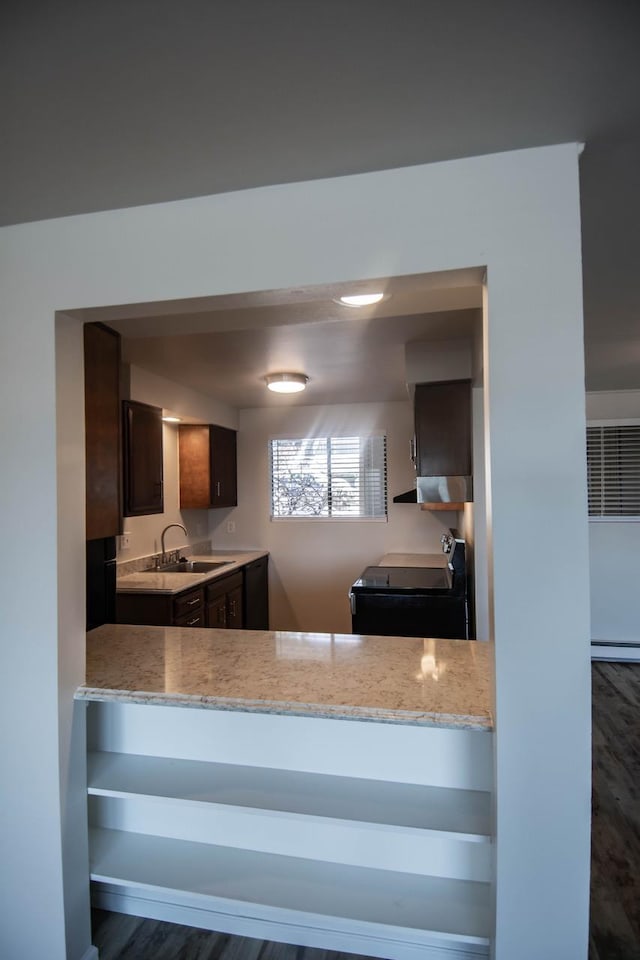 kitchen with sink, range, dark brown cabinets, light stone counters, and kitchen peninsula