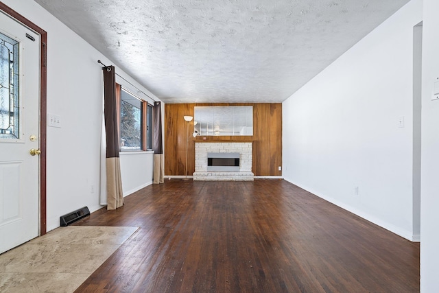 unfurnished living room with a brick fireplace, wooden walls, hardwood / wood-style floors, and a textured ceiling