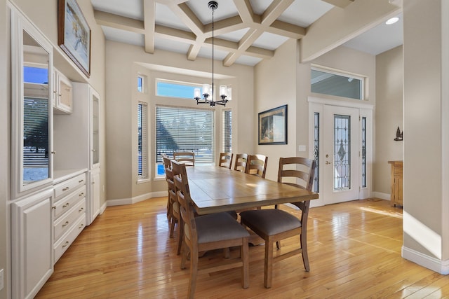 dining space with coffered ceiling, a notable chandelier, light wood-type flooring, and a towering ceiling