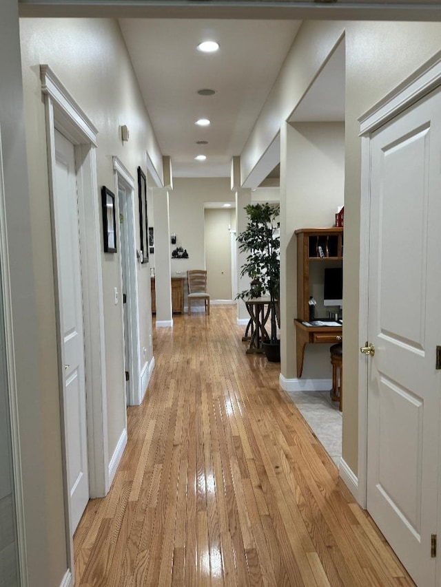 corridor featuring baseboards, light wood finished floors, and recessed lighting