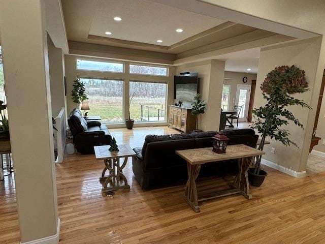 living room featuring a raised ceiling, baseboards, recessed lighting, and light wood-style floors