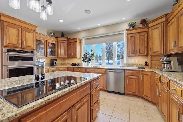 kitchen with a sink, stainless steel appliances, brown cabinetry, light stone countertops, and light tile patterned flooring