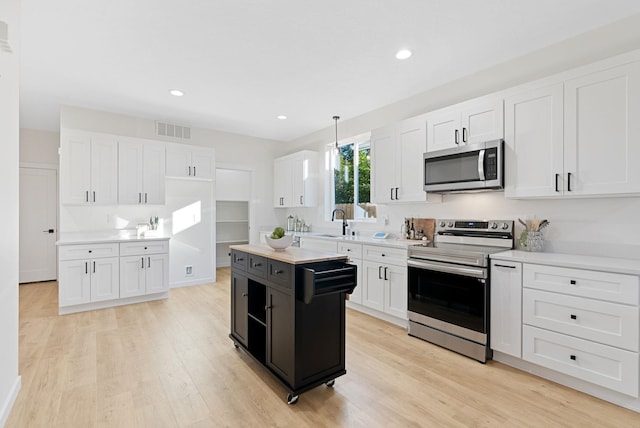 kitchen with white cabinetry, hanging light fixtures, light hardwood / wood-style flooring, and appliances with stainless steel finishes