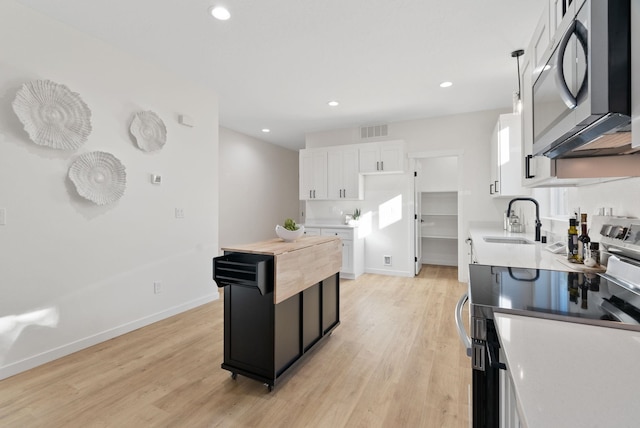 kitchen featuring appliances with stainless steel finishes, pendant lighting, white cabinetry, sink, and light hardwood / wood-style flooring