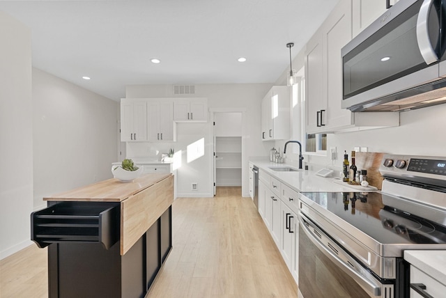 kitchen with sink, light hardwood / wood-style flooring, white cabinetry, hanging light fixtures, and stainless steel appliances