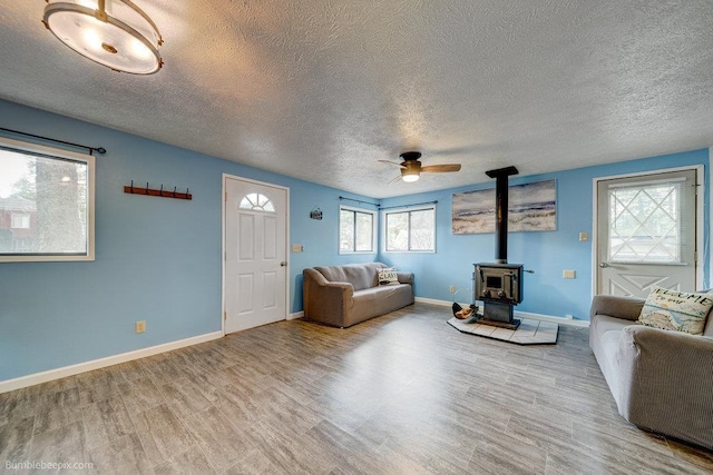 unfurnished living room featuring ceiling fan, a wood stove, a textured ceiling, and light hardwood / wood-style flooring