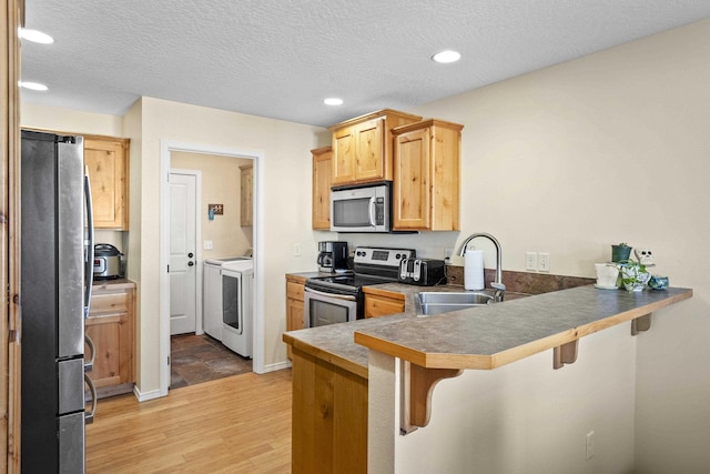 kitchen featuring sink, washing machine and dryer, kitchen peninsula, and appliances with stainless steel finishes