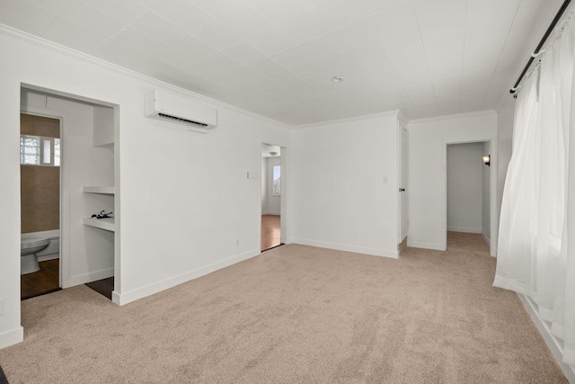 unfurnished bedroom with a wall mounted air conditioner, crown molding, ensuite bath, and light colored carpet