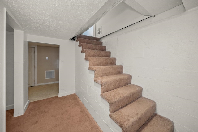 stairs featuring a textured ceiling and carpet flooring