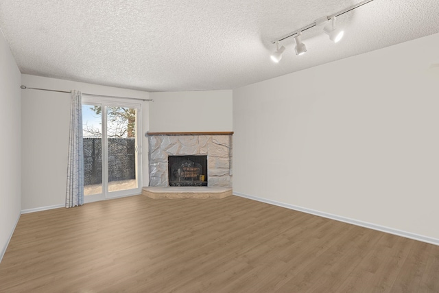 unfurnished living room with baseboards, wood finished floors, a textured ceiling, a stone fireplace, and track lighting