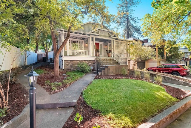 view of front of property featuring a front lawn, fence, stone siding, and covered porch
