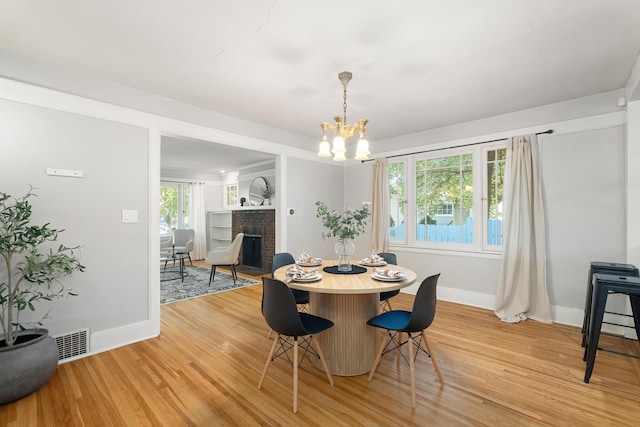 dining area with a brick fireplace, a notable chandelier, and light hardwood / wood-style flooring