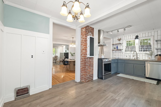 kitchen with a decorative wall, light wood-style flooring, stainless steel appliances, island range hood, and a notable chandelier