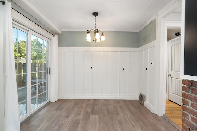 unfurnished dining area with a decorative wall, ornamental molding, wood finished floors, and an inviting chandelier