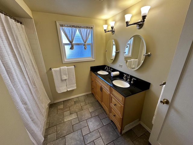 bathroom featuring stone tile flooring, double vanity, baseboards, and a sink