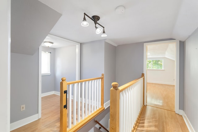 hallway featuring light wood finished floors, baseboards, vaulted ceiling, and an upstairs landing