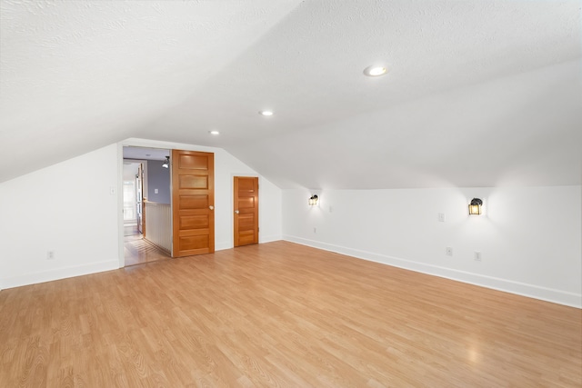 additional living space with vaulted ceiling, light hardwood / wood-style floors, and a textured ceiling