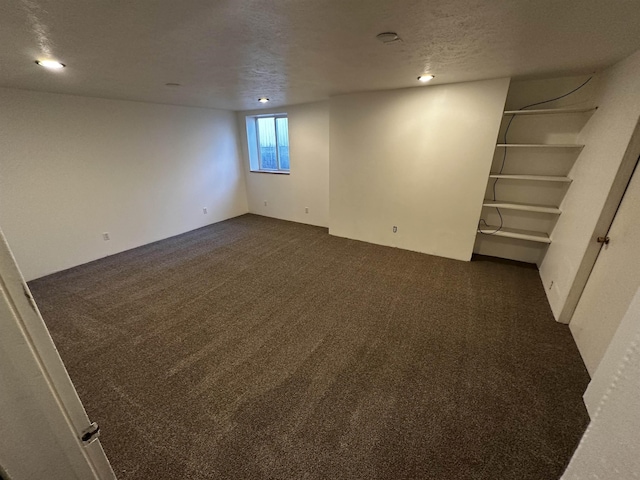 basement featuring dark carpet and a textured ceiling