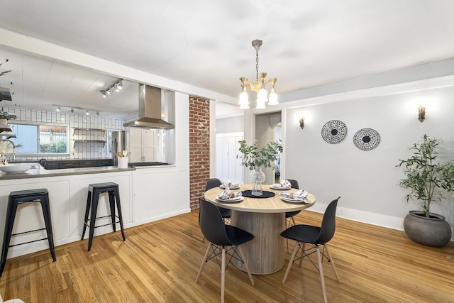 dining space featuring track lighting, light wood finished floors, baseboards, and an inviting chandelier