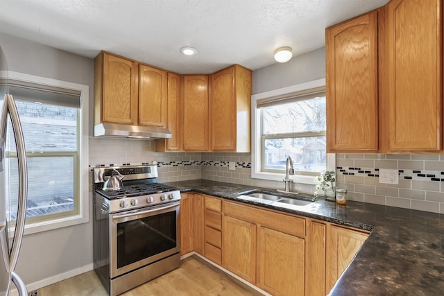 kitchen featuring sink, stainless steel gas range oven, dark stone counters, light hardwood / wood-style floors, and decorative backsplash