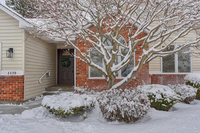 snow covered property entrance featuring brick siding