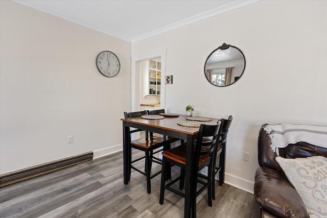 dining space with ornamental molding, wood-type flooring, and a baseboard heating unit