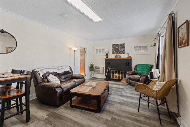 living room featuring hardwood / wood-style floors, a wall mounted AC, ornamental molding, a brick fireplace, and a textured ceiling