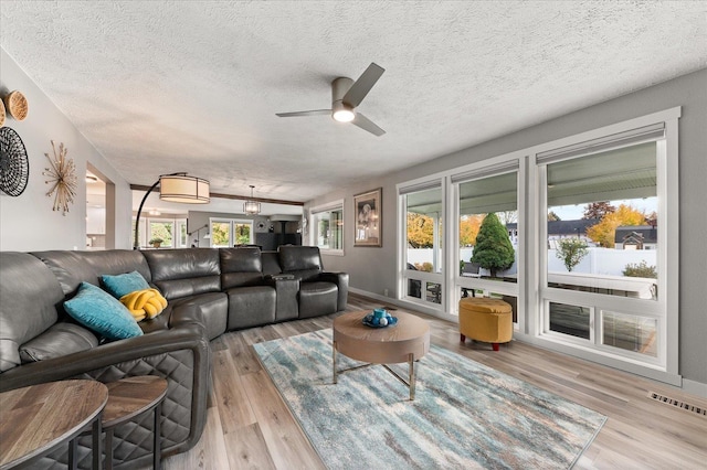 living room with ceiling fan, a textured ceiling, and light wood-type flooring