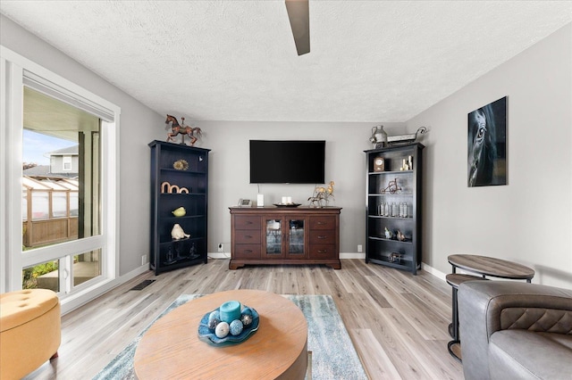 living room with ceiling fan, a textured ceiling, and light wood-type flooring