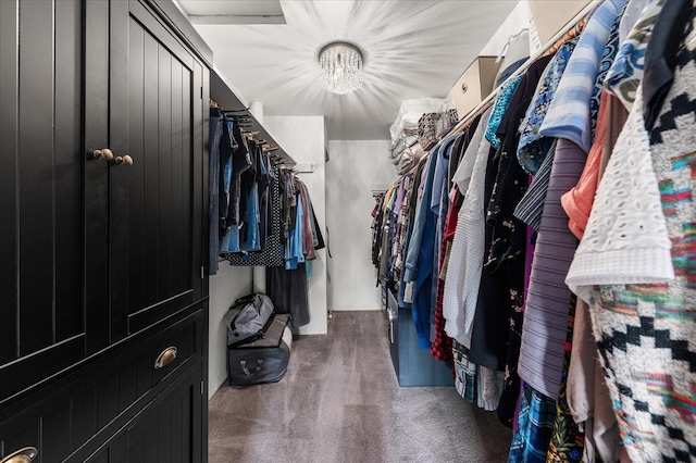 walk in closet with a notable chandelier and dark colored carpet