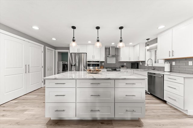 kitchen featuring wall chimney range hood, white cabinetry, stainless steel appliances, a center island, and washer / dryer