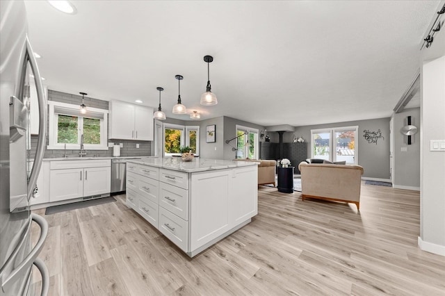 kitchen featuring white cabinetry, stainless steel appliances, a center island, light stone countertops, and light wood-type flooring