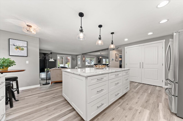 kitchen featuring white cabinetry, hanging light fixtures, stainless steel fridge, a kitchen island, and light stone countertops