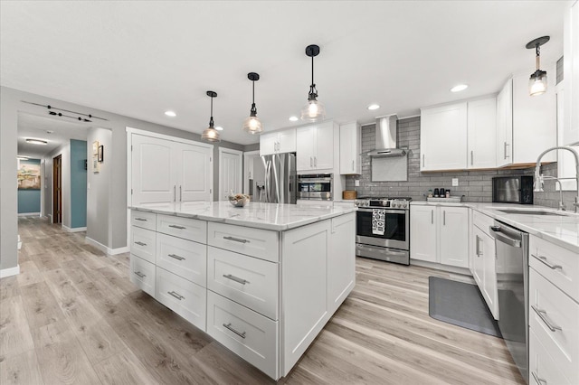 kitchen featuring wall chimney range hood, sink, white cabinetry, stainless steel appliances, and a center island