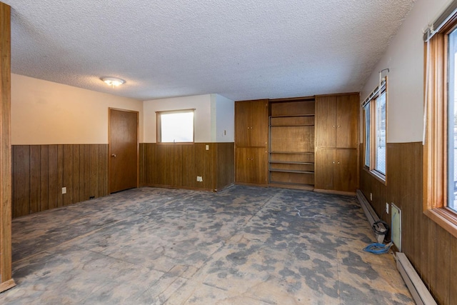 unfurnished room featuring a baseboard radiator, a textured ceiling, and wood walls