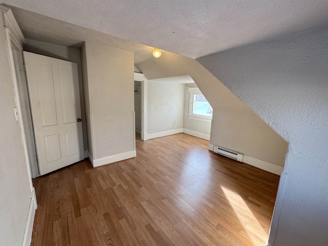 bonus room with lofted ceiling, wood-type flooring, a textured ceiling, and a baseboard heating unit