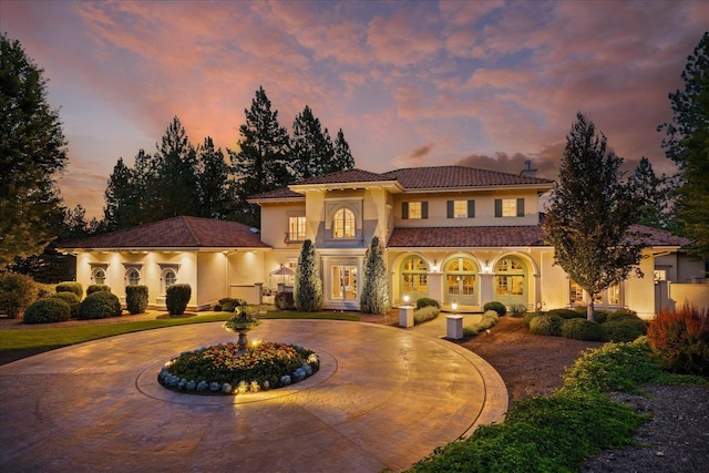 mediterranean / spanish home with stucco siding, curved driveway, french doors, and a tiled roof