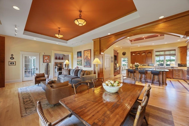 dining space with a raised ceiling, sink, and light hardwood / wood-style flooring