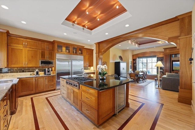 kitchen featuring built in appliances, a raised ceiling, dark stone countertops, and a center island